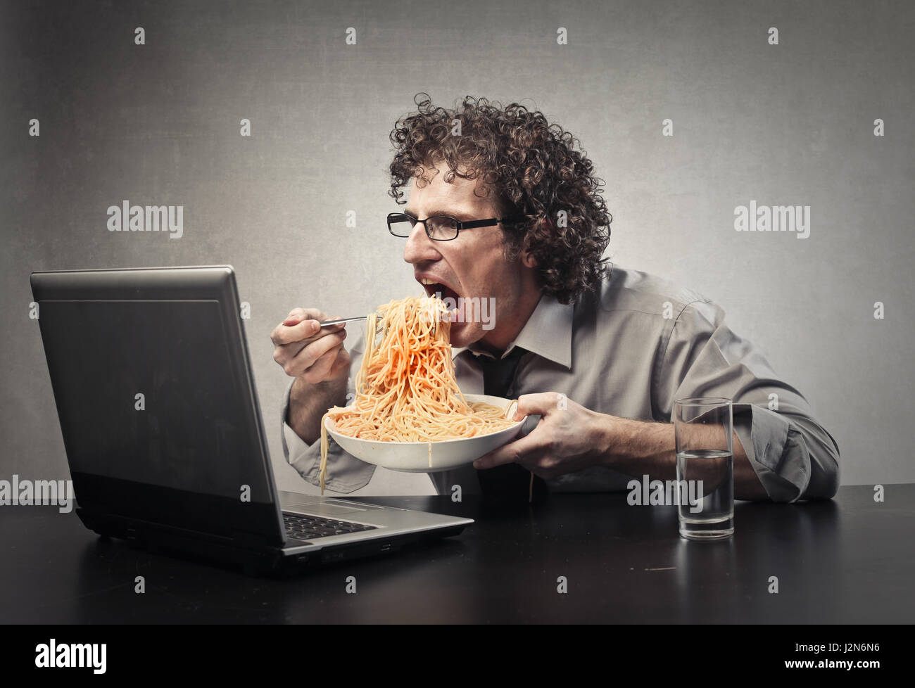 Man eating pasta in front of laptop Stock Photo