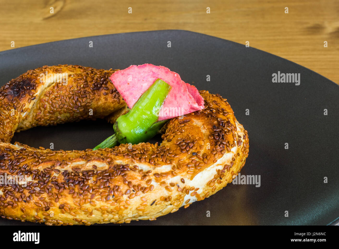 Closeup of traditional Turkish Pastry (Simit) with salami served on a grey plate on a wooden table Stock Photo
