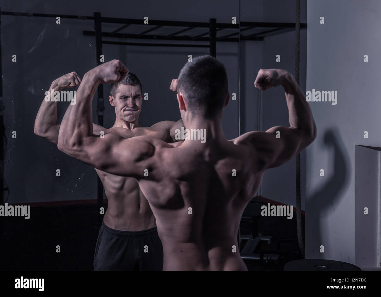 Back view of strong female athlete reflecting in mirror in gym and