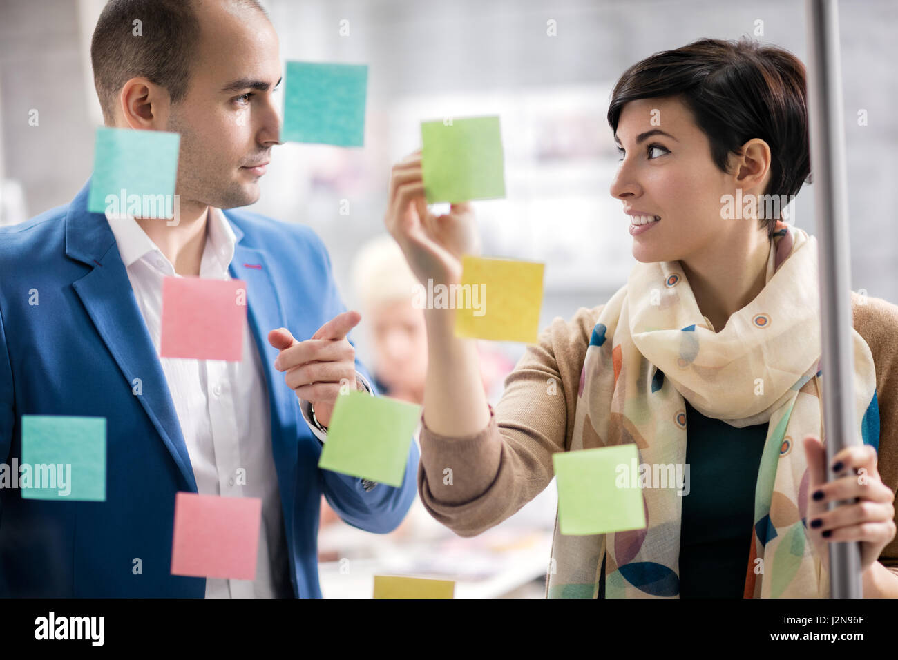 Colorful stickers on glass panel help female designer and her associate in job Stock Photo
