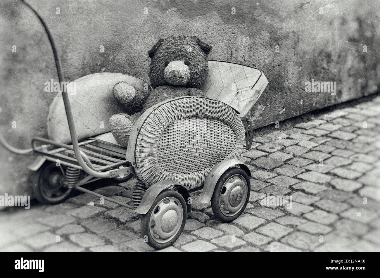 Old dirty Teddy bear toy sitting in the retro baby carriage on the street - lost lonely children concept, vintage hipster grunge image, black and whit Stock Photo