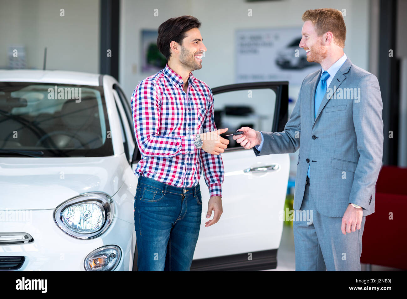 Sales situation in a car dealership, the dealer giving key of car at young male, Stock Photo