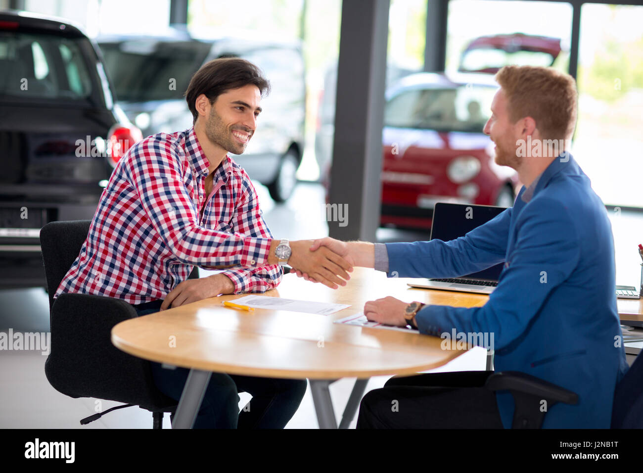 Man at a car dealership buying an auto, car agent handshake with his client Stock Photo