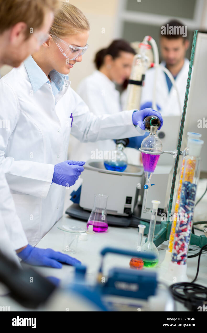Cute female chemist doing experiment mixing liquids in chemical lab