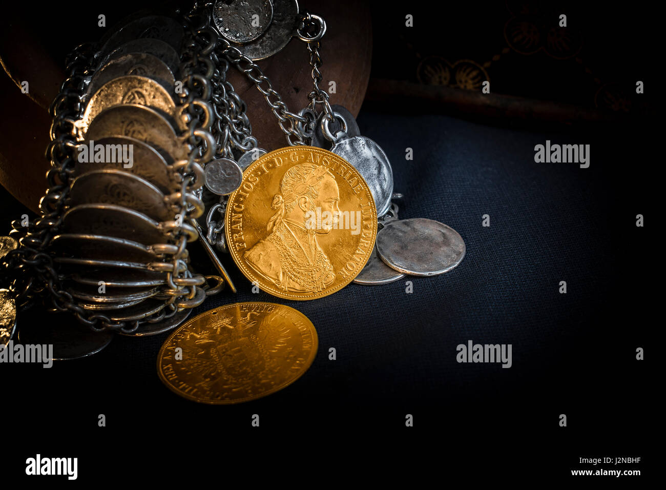 Still Life with two Austria-Hungary thalers, avers and revers of golden coin-ducats from 1915 with Kaiser Franz Joseph I, leaning on silver jewelery a Stock Photo