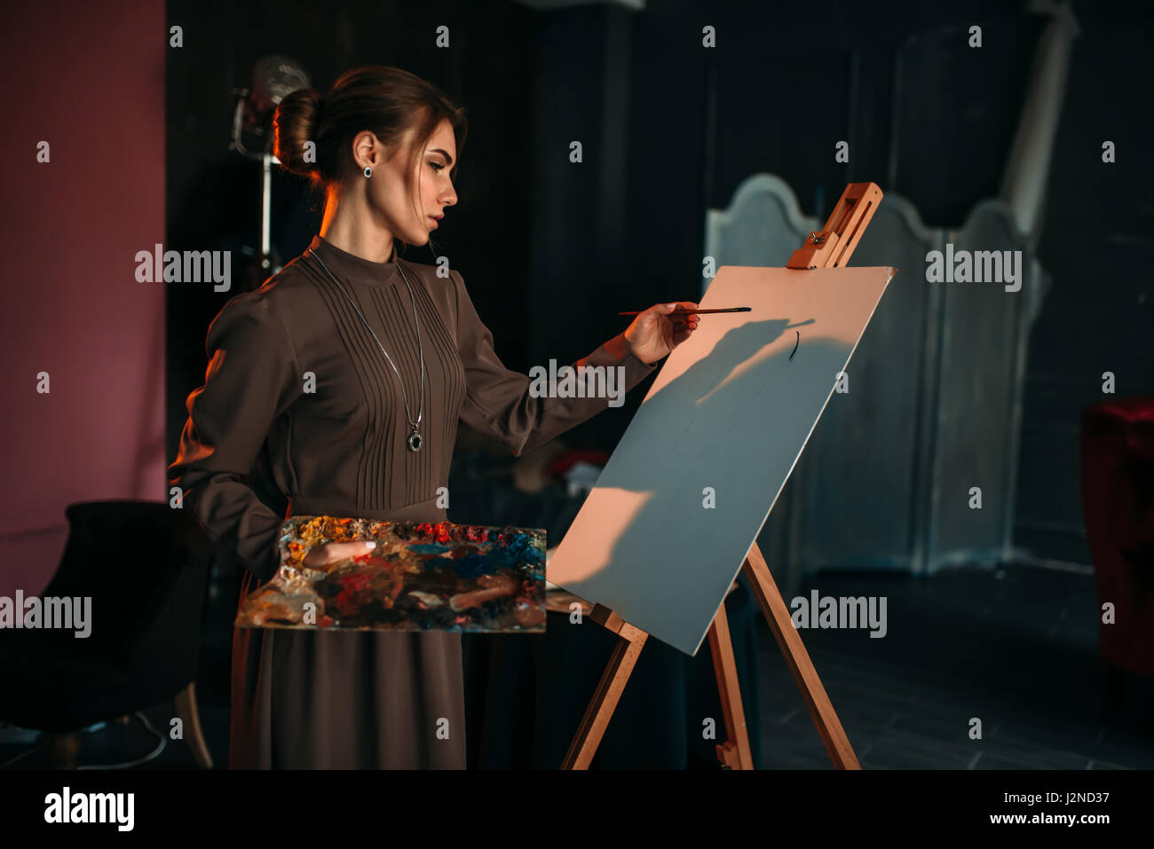Female painter with brush and palette in hands in art studio. Oil paint ...