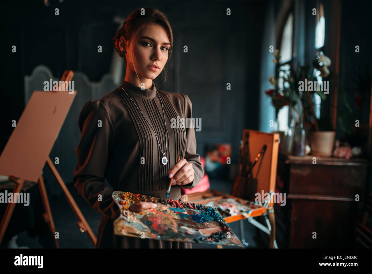 Female painter with brush and palette in hands in art studio. Oil paint ...