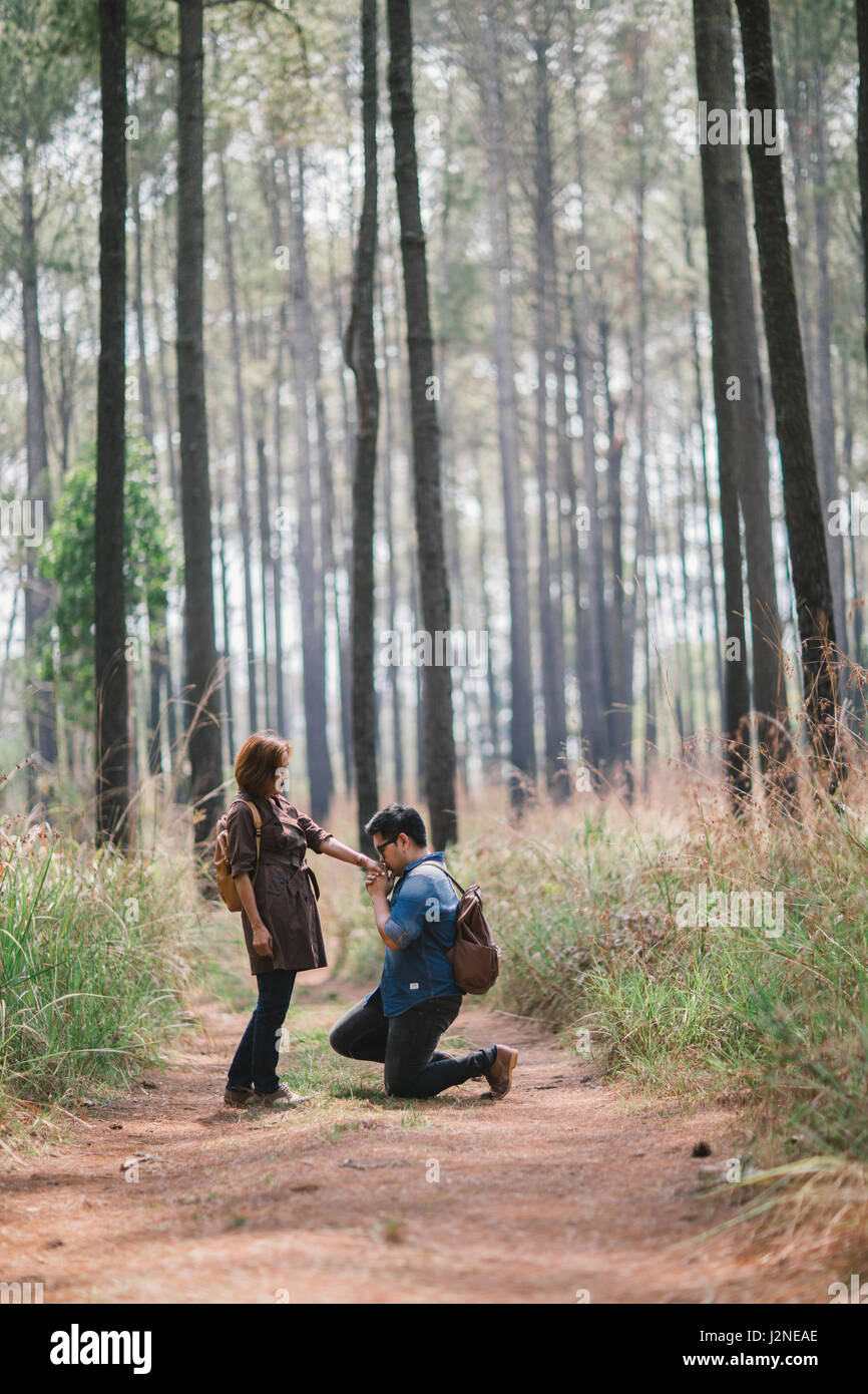 An Asian man make a romance down on one knee proposal in the pine