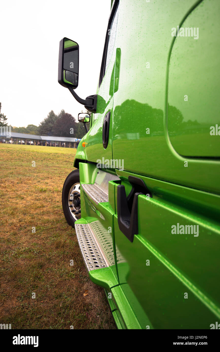 Side modern green semi truck with a shiny reflective paint everything as in a mirror with aluminum footrest, a mirror and a wheel on the grass parking Stock Photo