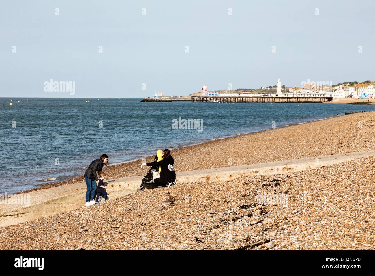 Herne Bay, Kent, UK. 29th April, 2017. UK Weather News.  A sunny evening on the first day of Mayday Bank Holiday weekend enables people to go to the beach although they remain wrapped up against the cold. Two young women sit on the beach with a small child. Credit: Richard Donovan/Live Alamy News Stock Photo
