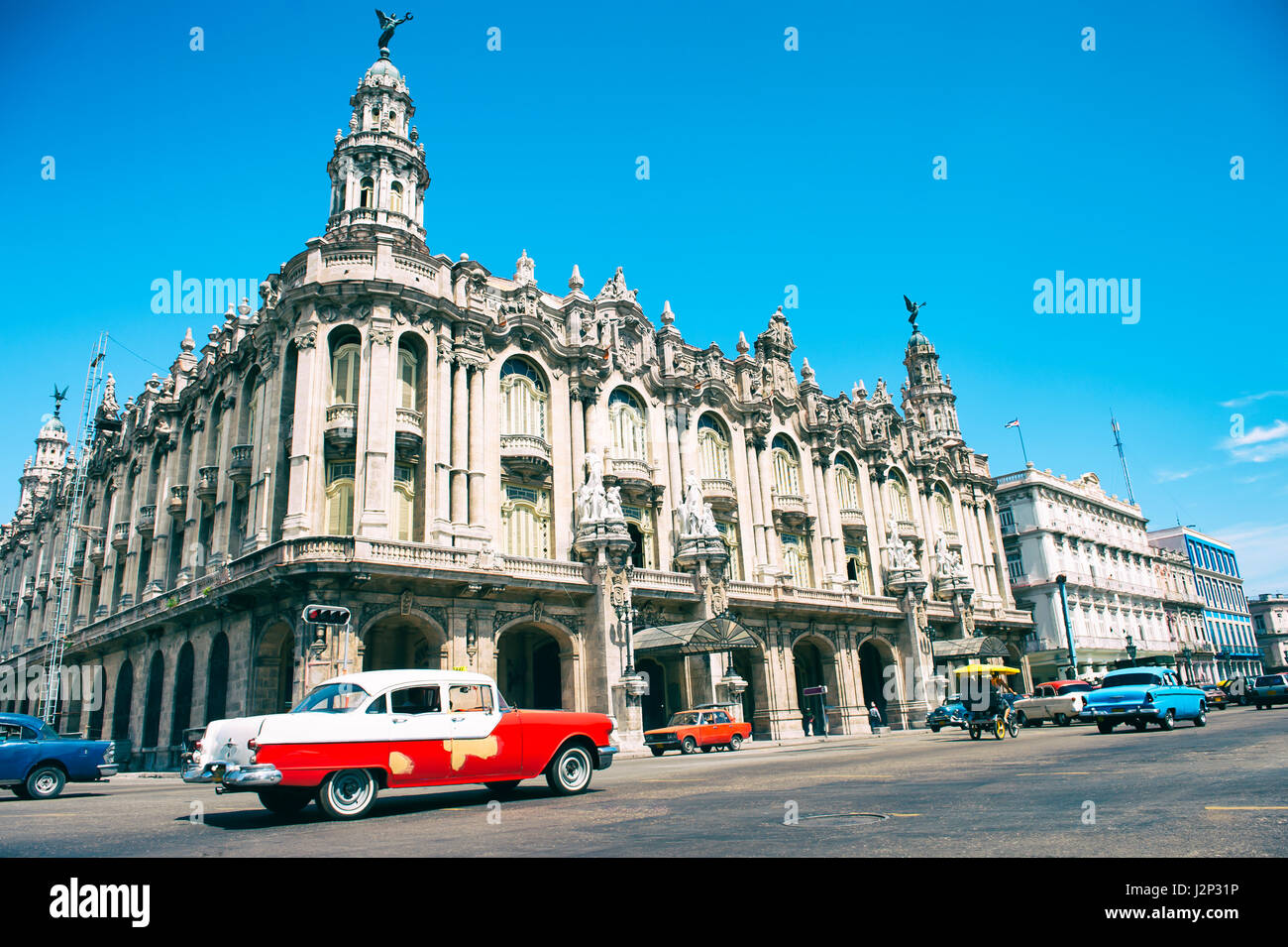 HAVANA - JUNE 14, 2011: Classic American cars serving as taxis drive in front of a bright view of the landmark Great Theatre of Havana. Stock Photo