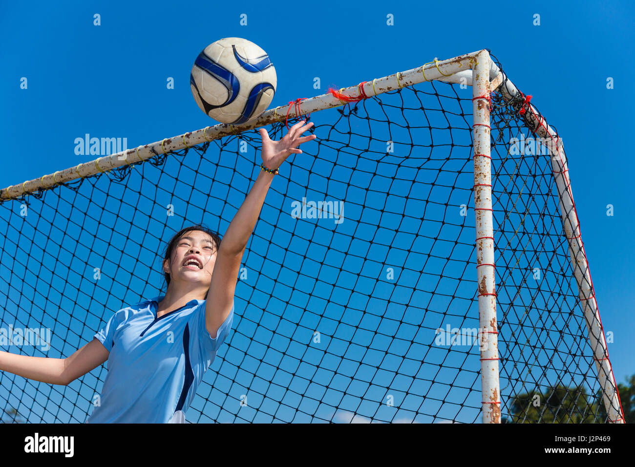 young asian girl goalkeeper catching the ball during a fun practice in a field on a clear blue sky day Stock Photo