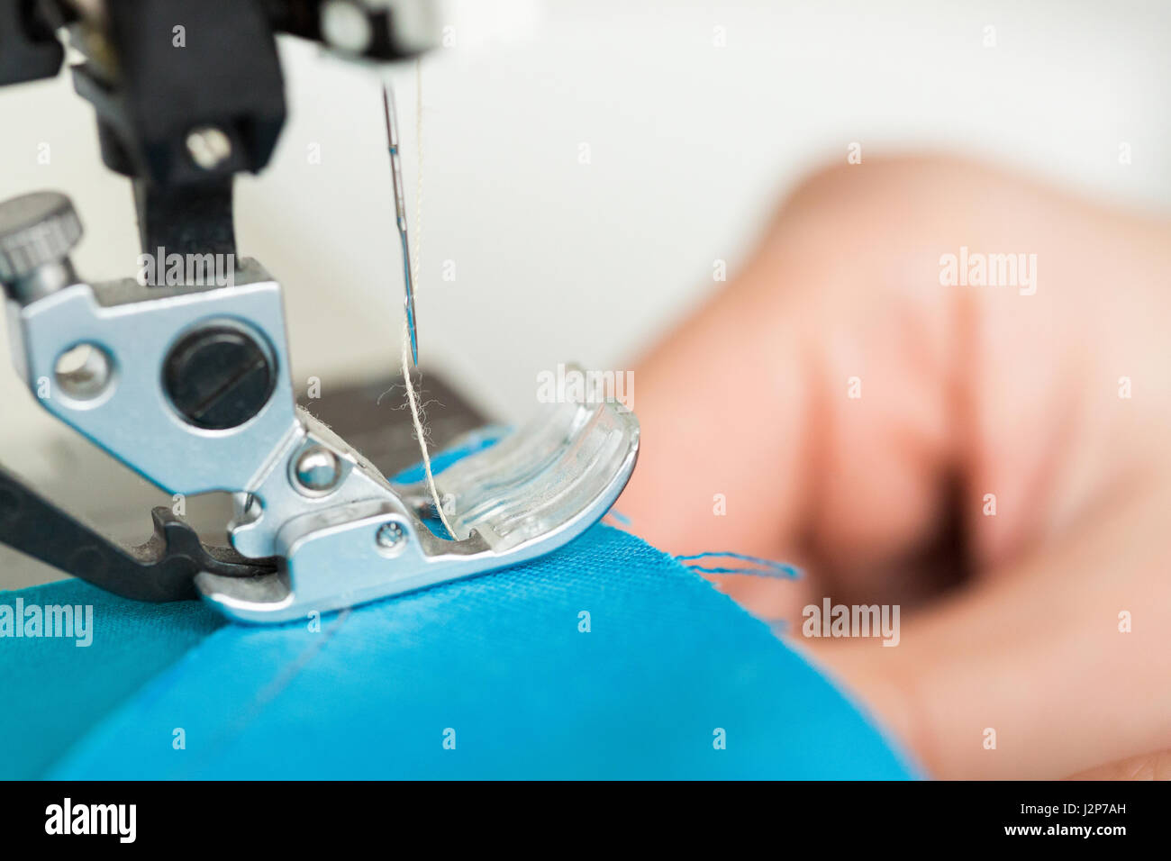 needlework and quilting in the workshop of a tailor - closeup on the needle of sewing machine stitches the pieces of colored blue fabric. Stock Photo