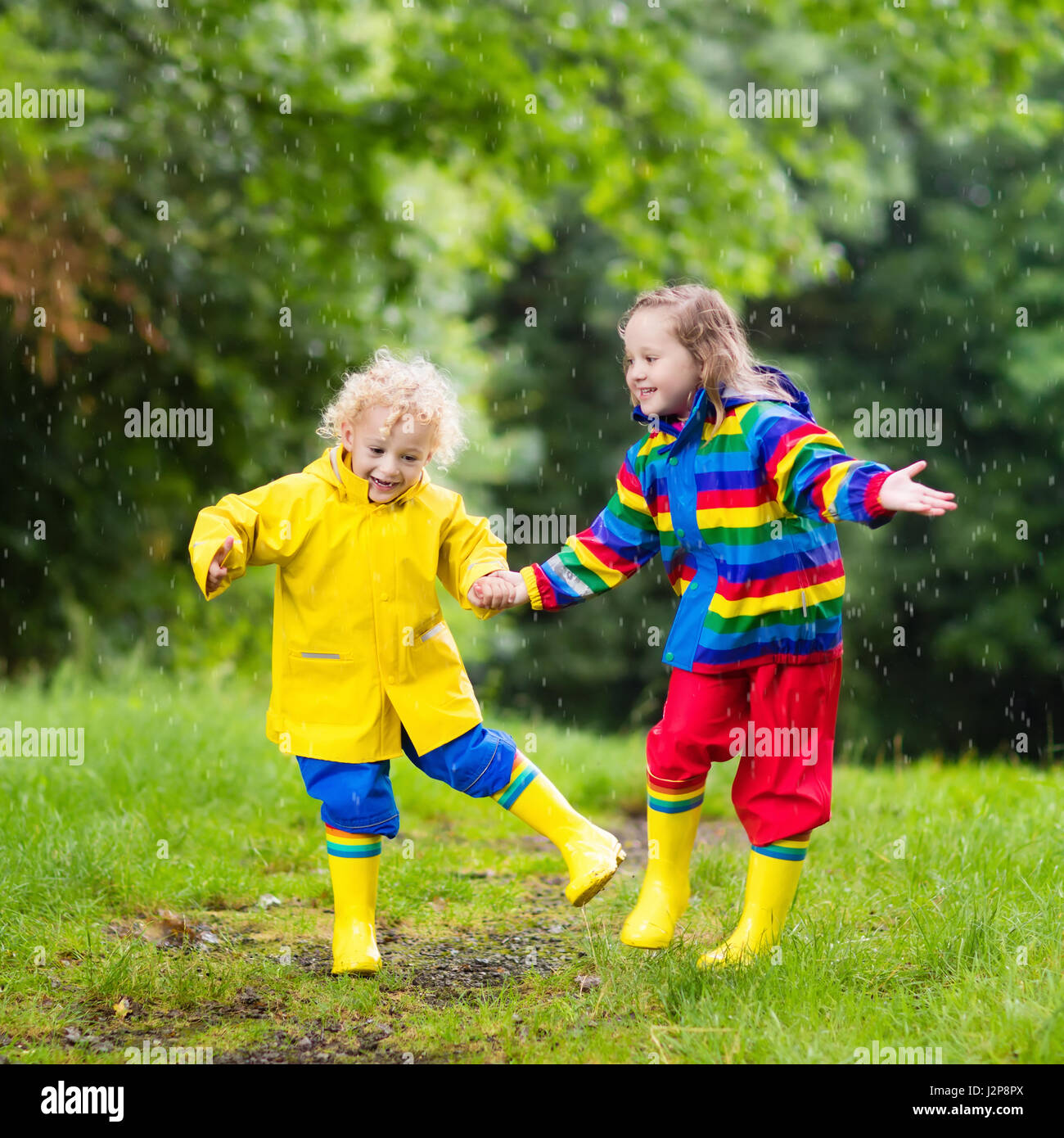 Little boy and girl play in rainy summer park. Children with colorful