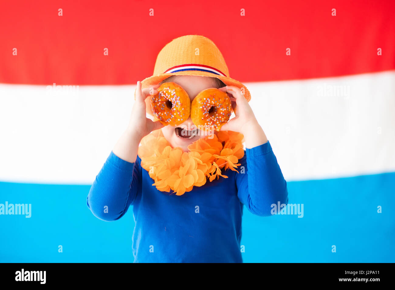 Little Dutch boy girl wearing country symbols eating orange donuts celebrating King day. Children support Holland sport team. Kids from the Netherland Stock Photo