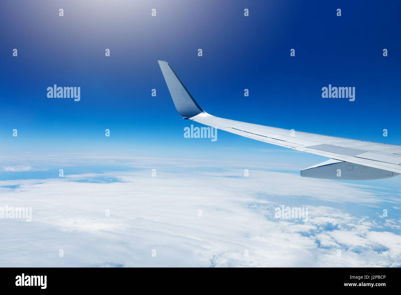 wing of an airplane flying high in the sky above the clouds Stock Photo