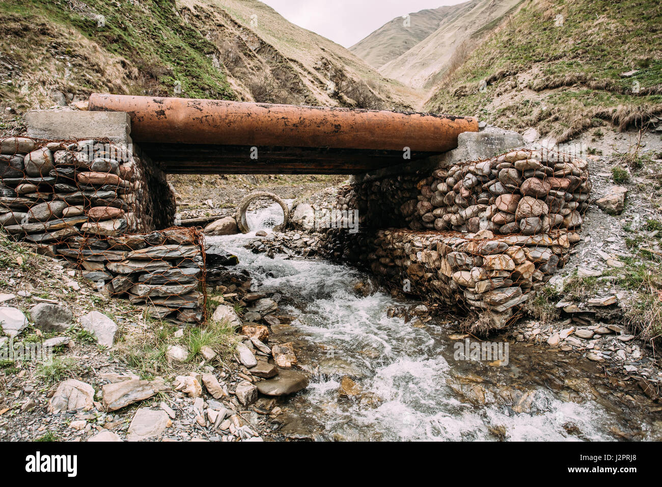 Small Bridge Through Terek River In In Truso Gorge, Kazbegi District, Mtskheta-mtianeti Region, Georgia. Spring Or Summer Season Stock Photo