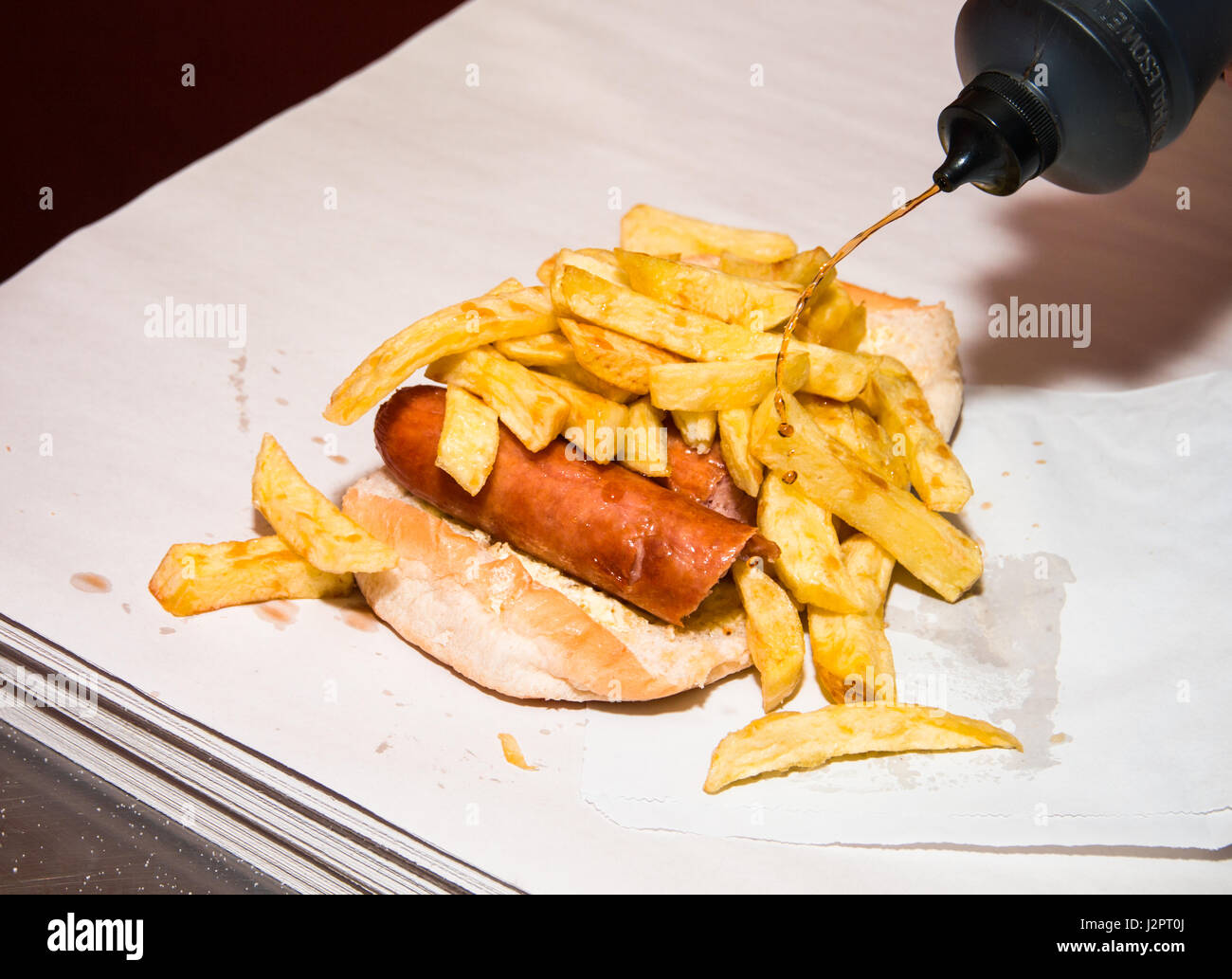 Vinegar being squirted on sausage and chips on a muffin in a fish and chip shop Stock Photo Alamy