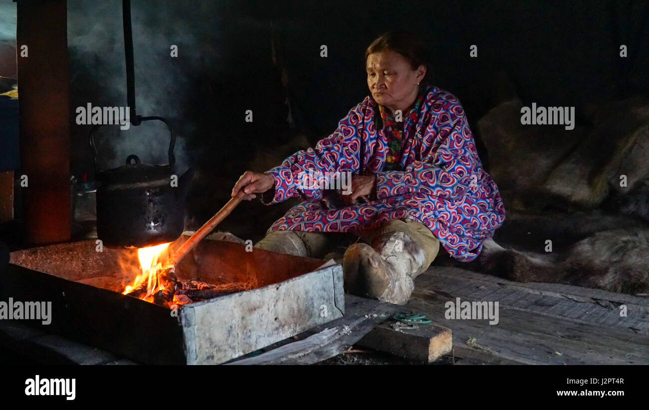 Nenets woman inside the chum sitting by the fire with a kettle. Summer Stock Photo
