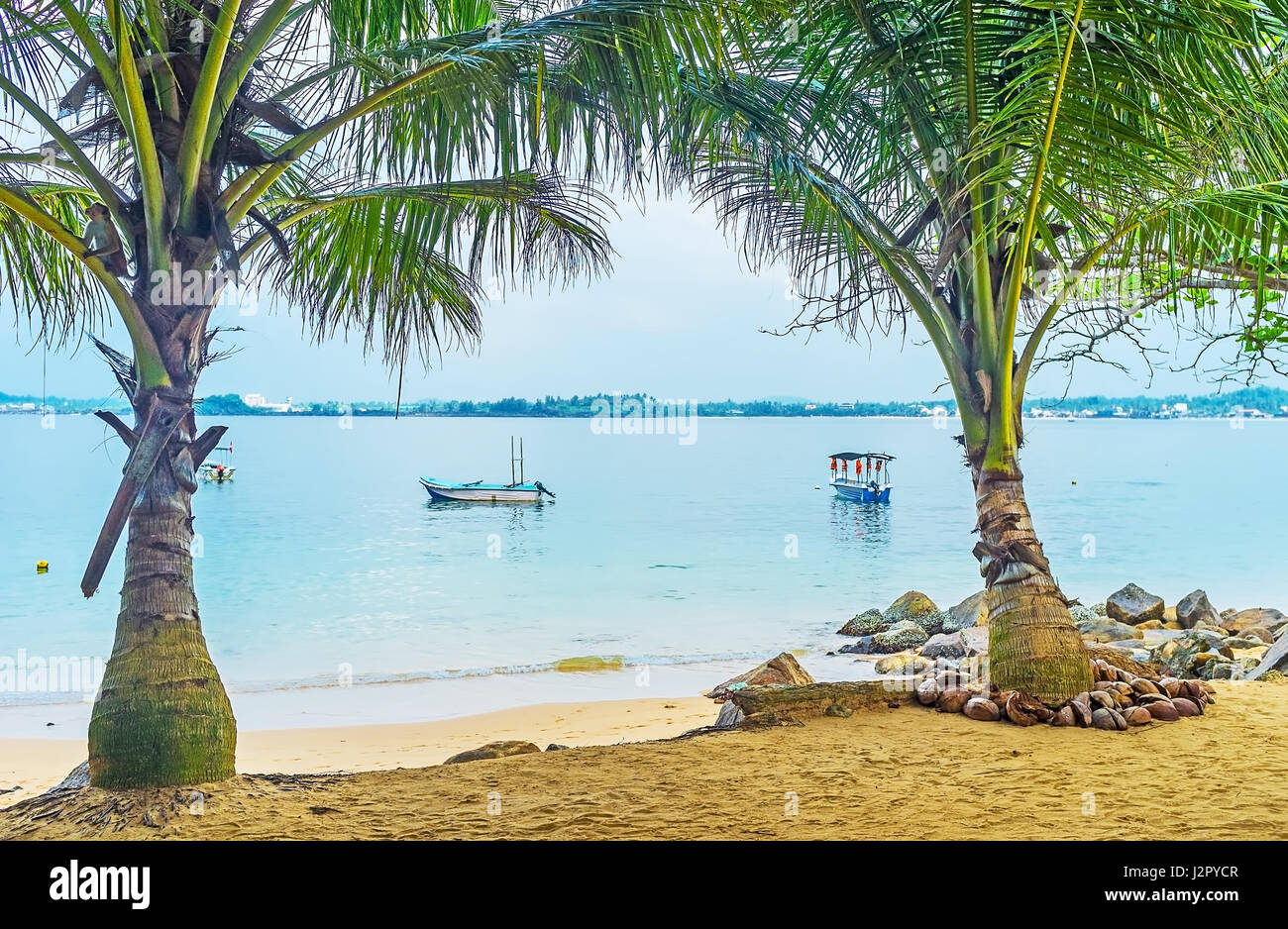 The view on the shore of Jungle Beach with pleasure boats through the shady palms on the sand, Unawatuna, Sri Lanka. Stock Photo