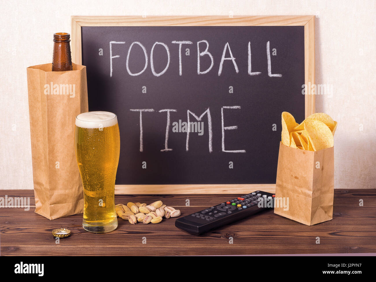 football fans setting of beer bottle in brown paper bag,  glass, chips, pistachio, tv remote control and handwriting text football time written in cha Stock Photo