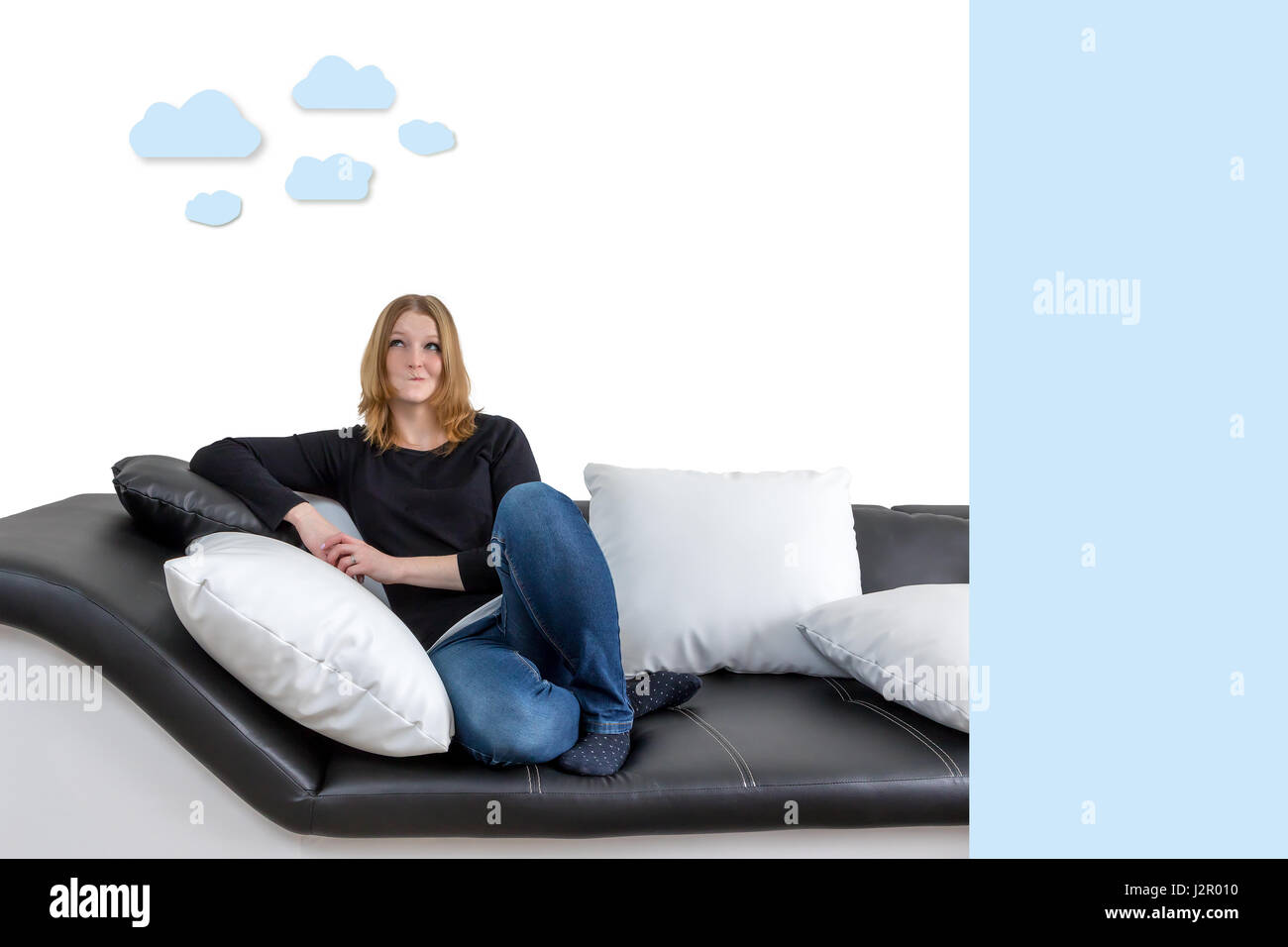 Grinning long haired young woman is sitting on a black and white couch with black and white pillows. Woman is looking upwards on the illustration of c Stock Photo