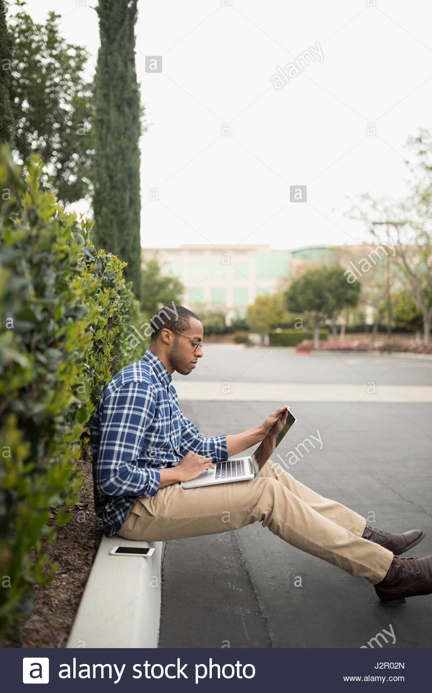 African American businessman using laptop outside office building Stock