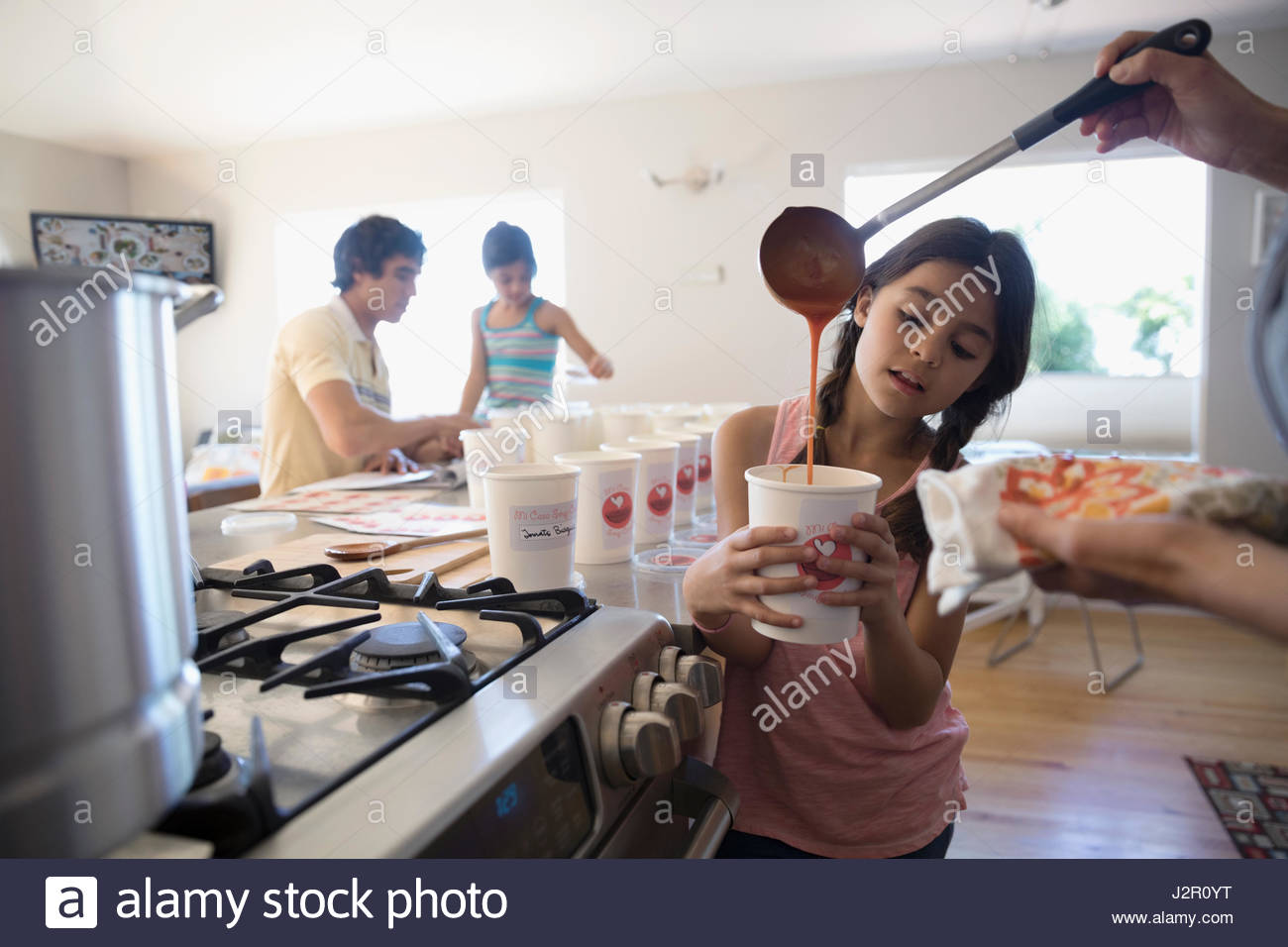 Mother and daughter cooking soup, pouring into container in kitchen Stock Photo