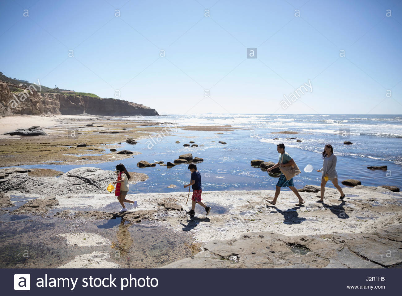 Latino family walking on craggy sunny beach Stock Photo