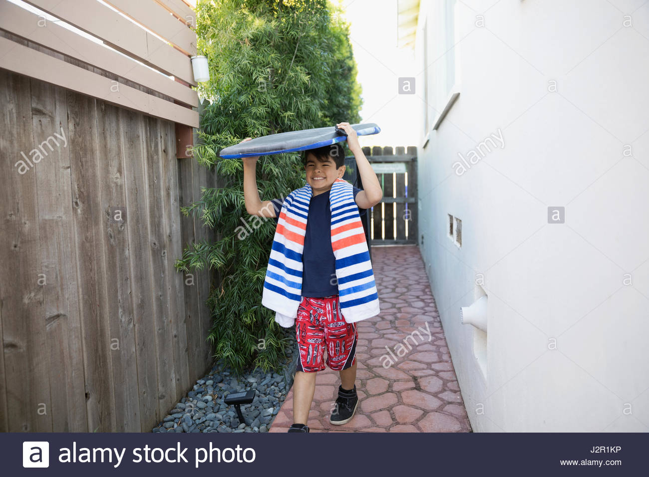 Enthusiastic Latino boy running with body board along house Stock Photo
