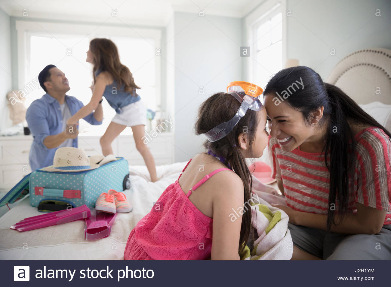 Playful mother and daughter rubbing noses on bed, packing for vacation Stock Photo