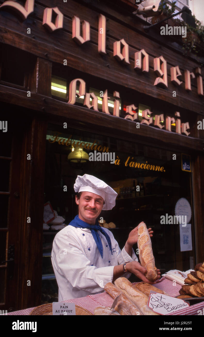 BOULANGERIE BAGUETTE BAKER PATISSERIE FRANCE French baker cap posing with freshly baked Baguette, outside with his bread market stall Honfleur France Stock Photo