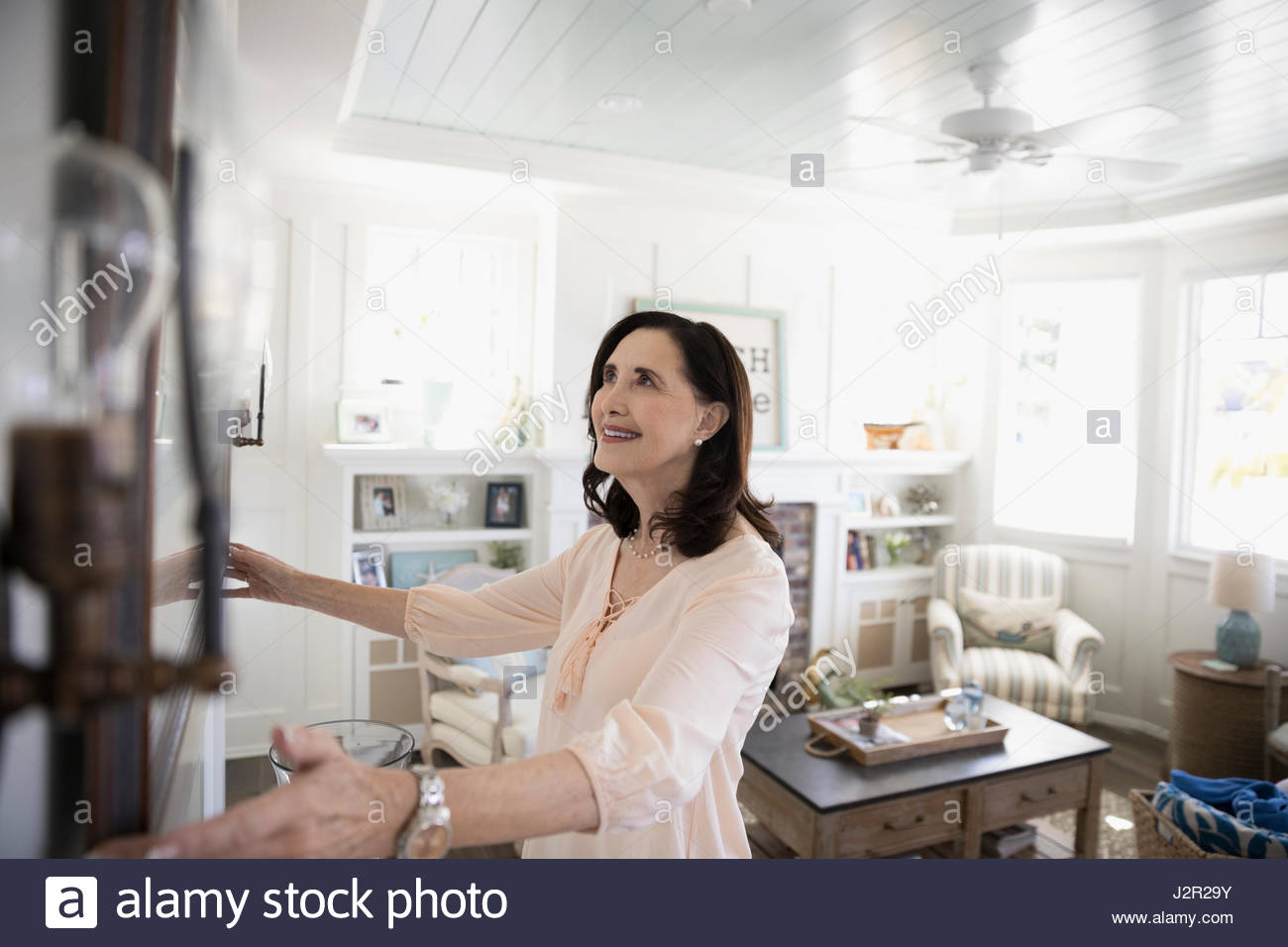 Woman hanging picture frame on beach house wall Stock Photo