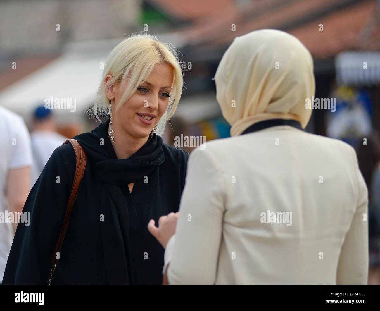A blonde girl talks to her muslim friend Stock Photo