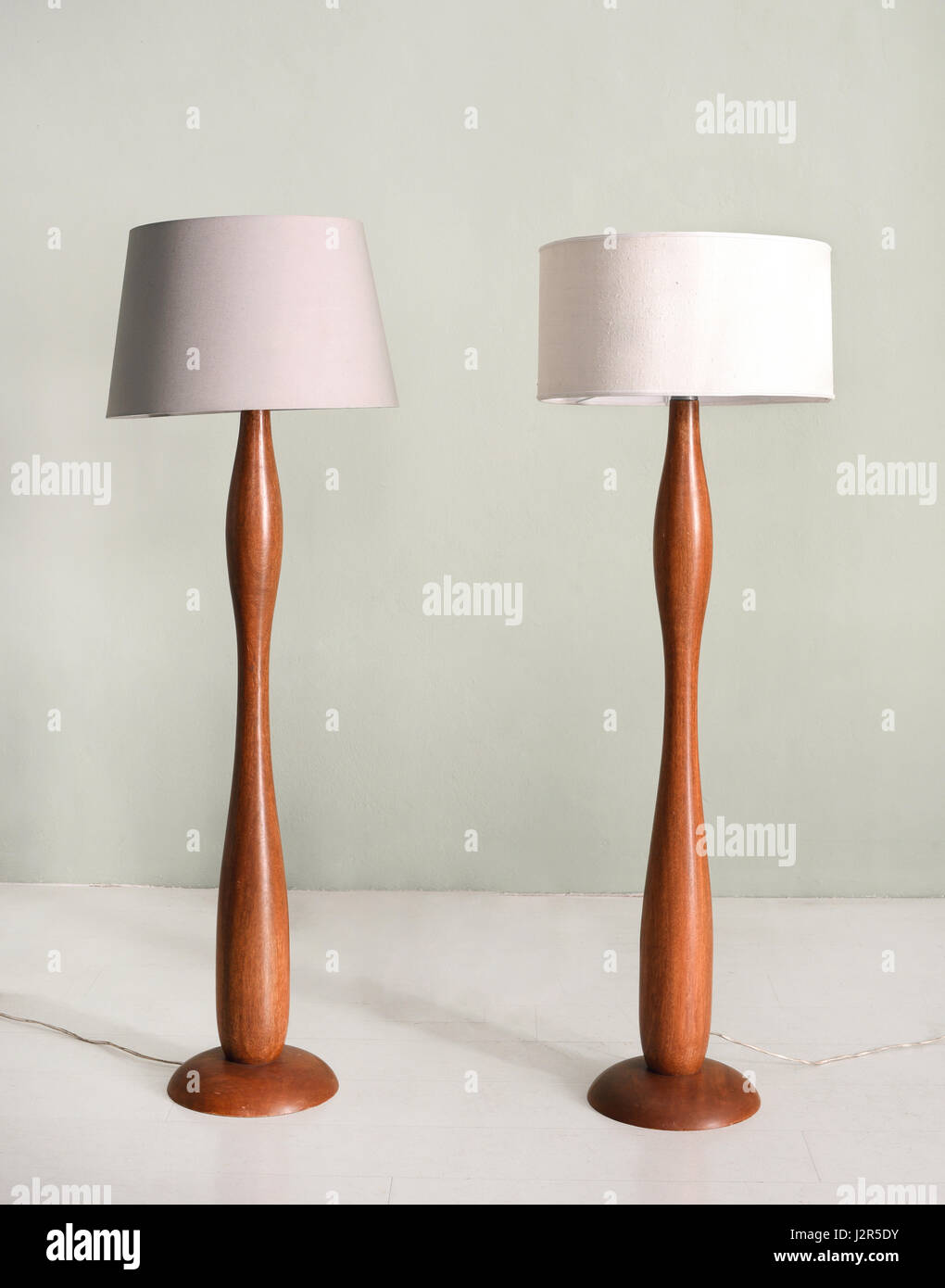 Pair of wooden floor or standing lamps with a curving sinuous shape and neutral colored cylindrical lampshades in a decor and design concept Stock Photo