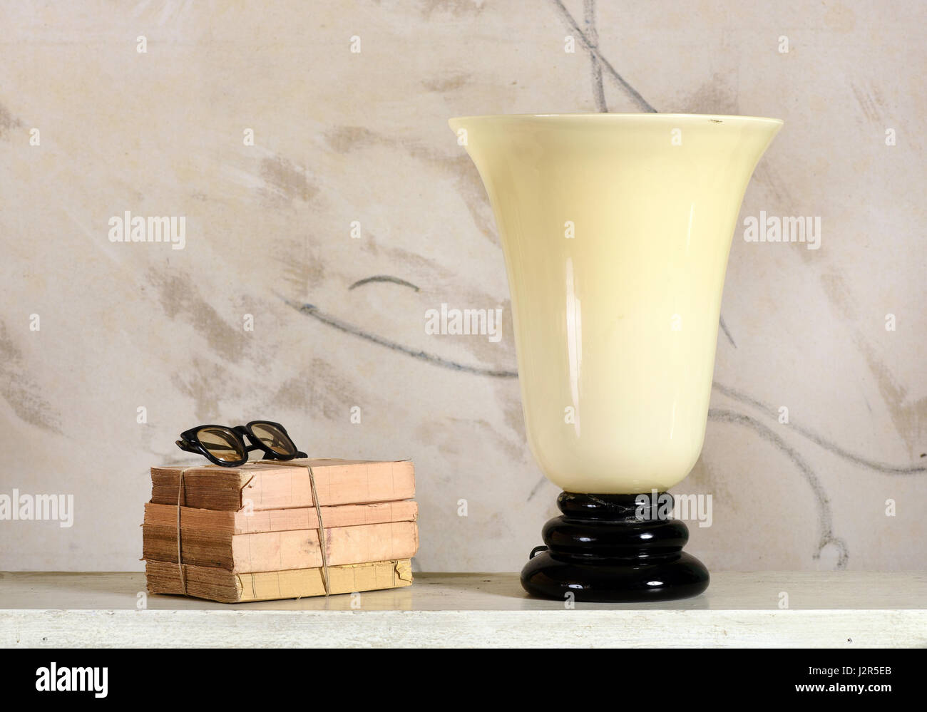 Trumpet shaped vintage uplighter lamp with opaque white glass in a black pedestal alongside a oile of old books toed with string with spectacles Stock Photo
