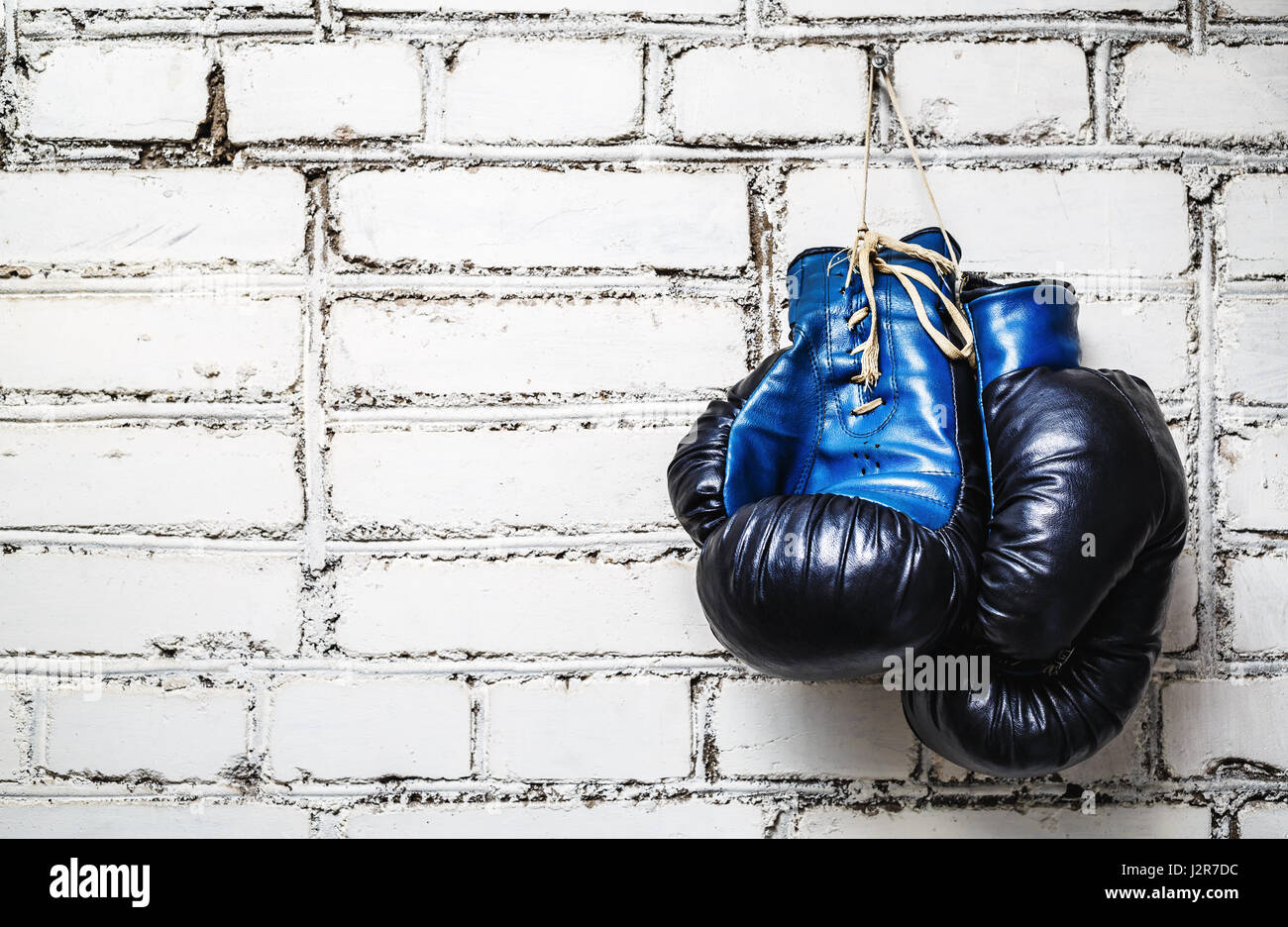 Pair of old blue and black boxing gloves hanging on white brick wall