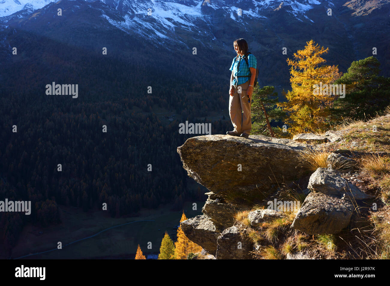Woman hiker enjoying view into Saas valley from rock, autmn, Saas Grund. Valais alps, Switzerland Stock Photo