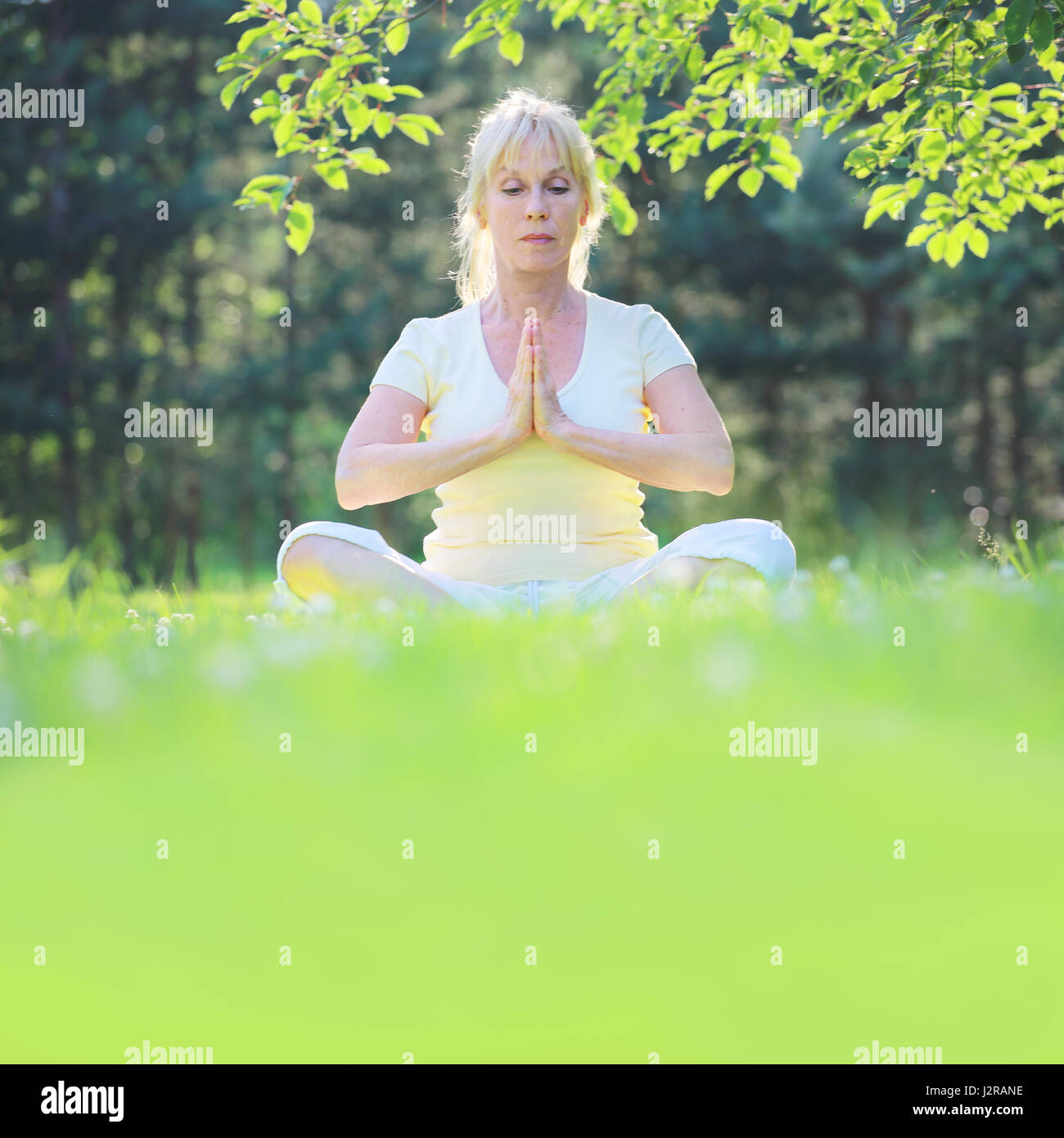 Beautiful mature woman in lotus yoga position in summer park Stock Photo