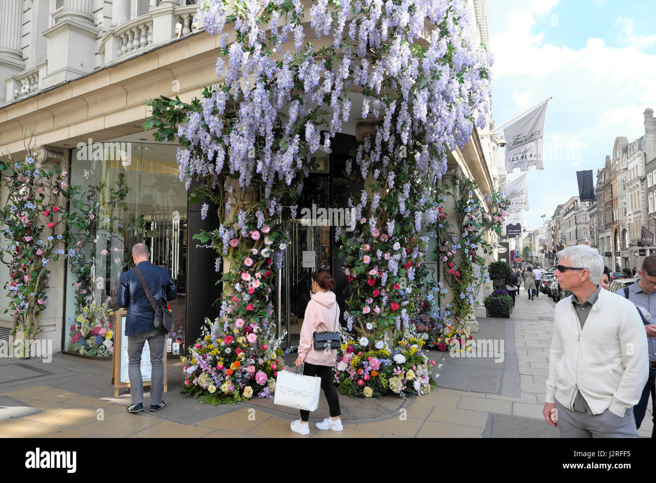 Artificial flowers with wisteria greet shoppers at the entrance of Fenwick's department store at  Brook St and New Bond Street London UK  KATHY DEWITT Stock Photo