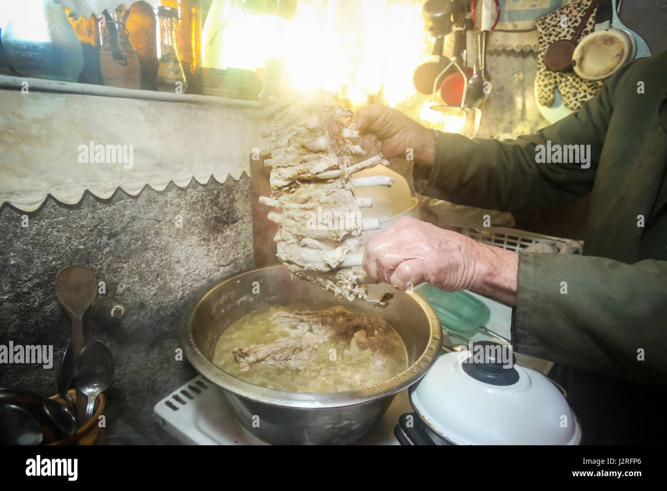 An old man boiling pork meat on the stove and holding a piece of ribs ...
