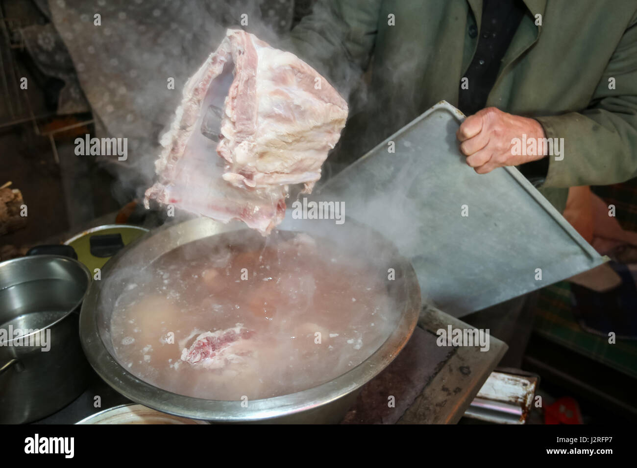 An old man boiling pork meat on the stove and holding a piece of ribs ...