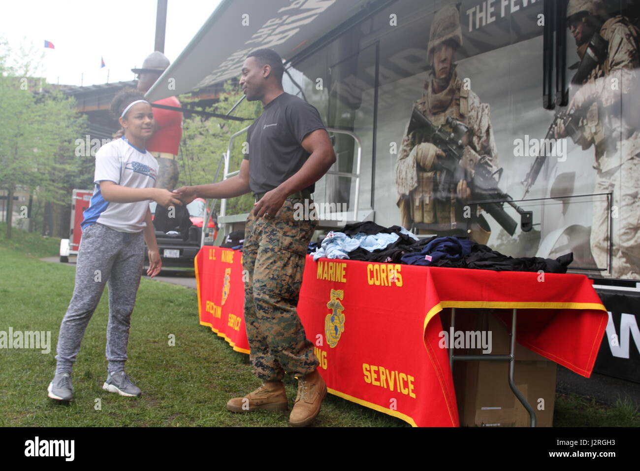SSgt. Lonny Washington-Paige, a recruiter with Recruiting Sub-Station Tun Tavern, hands a Marine shirt to Ciara Thomas, an athlete, April 29, 2017, in Philadelphia, Pennsylvania, during the 2017 Penn Relays. The Marines handed out hundreds of shirts, protein shakers, water bottles, hats, keychains, pencils, and racing jackets to athletes throughout the three day event. In order to receive an item, athletes had to perform pull-ups or a flexed-arm hang on the pull-up bar. (photo by Sgt. Matt Myers/Released) Stock Photo