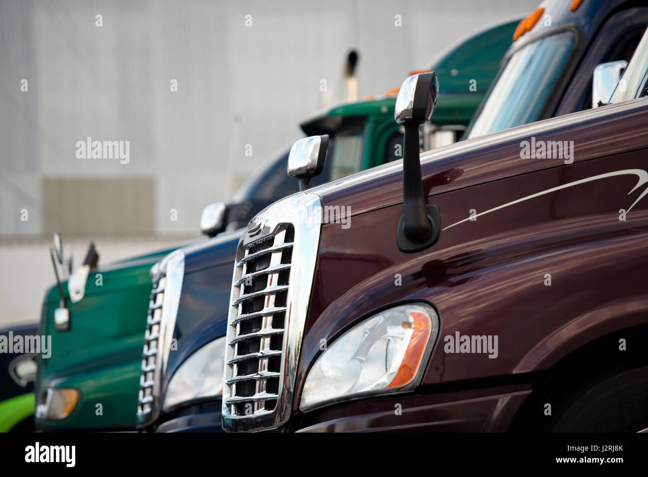 Chrome grille and headlights stylish and modern mirrors and hood with glass booths modern semi trucks of different coulors lined up on a platform Stock Photo