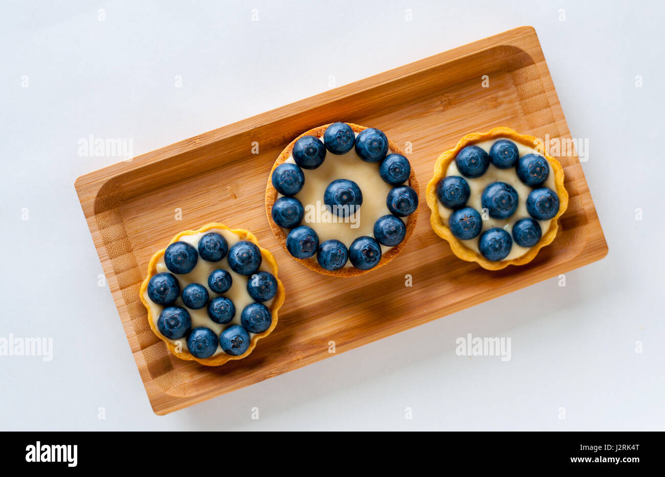 Three tarts with Blueberries served on wooden rectangular plate Stock