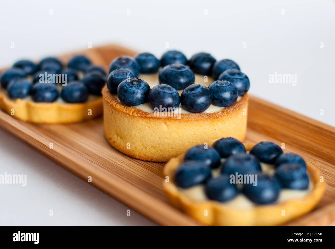 Three tarts with Blueberries served on wooden rectangular plate Stock