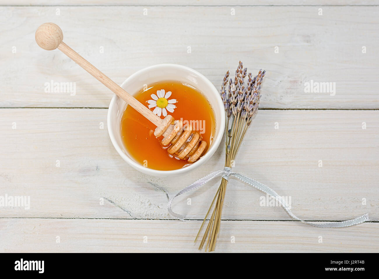 Bowl filled with flower honey with chamomile flower, decorated with a dried lavender bouquet Stock Photo