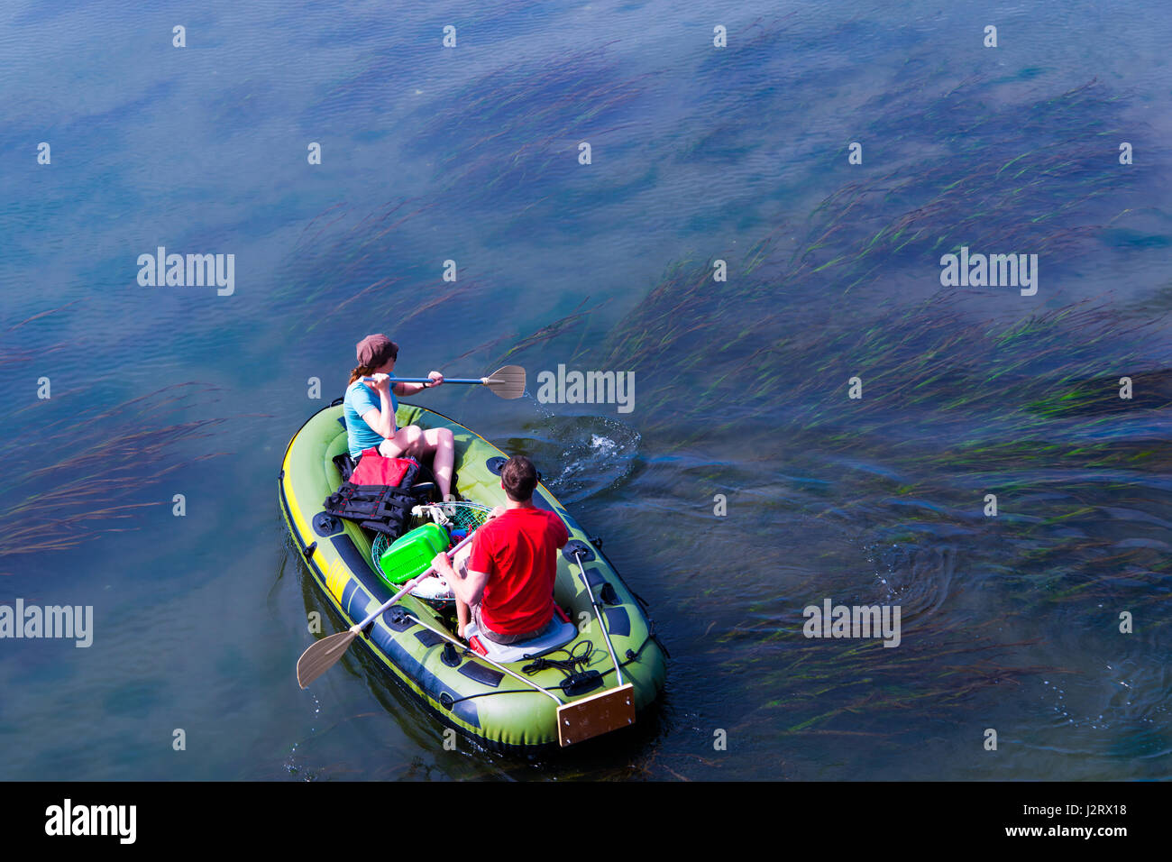 A man and a woman rowing oars while sitting in a rubber boat with gear
