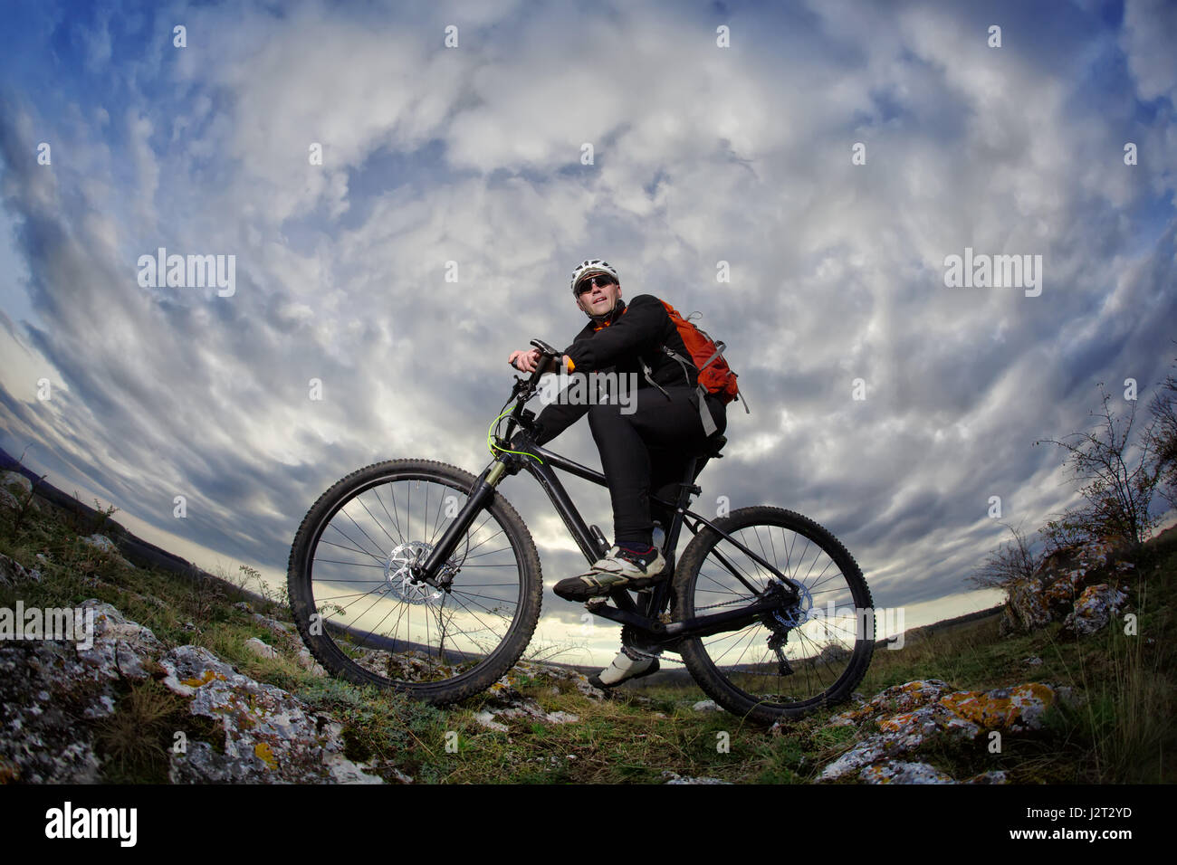 Portrait of the young cyclist standing with bike on the rocks against ...