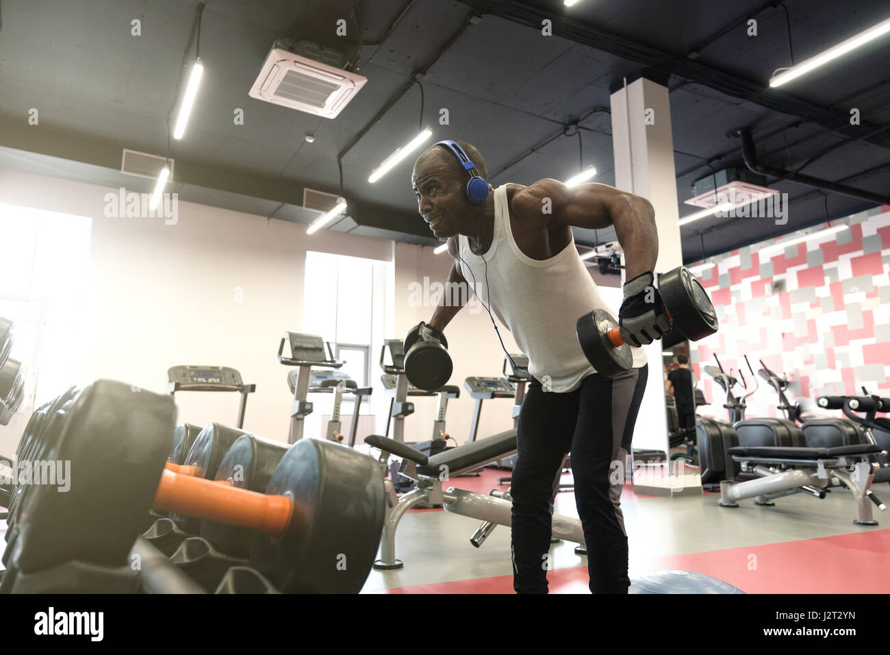 hard workout. Muscular black man wearing sportswear doing exercises with  dumbbells for back at gym Stock Photo - Alamy